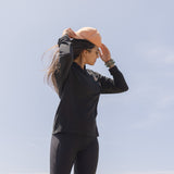 White Sands - Women's Long-Sleeve Hooded Henley in Obsidian (Black), person standing in a mountainous landscape.