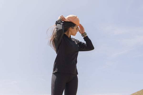 White Sands - Women's Long-Sleeve Hooded Henley in Obsidian (Black), person standing in a mountainous landscape.