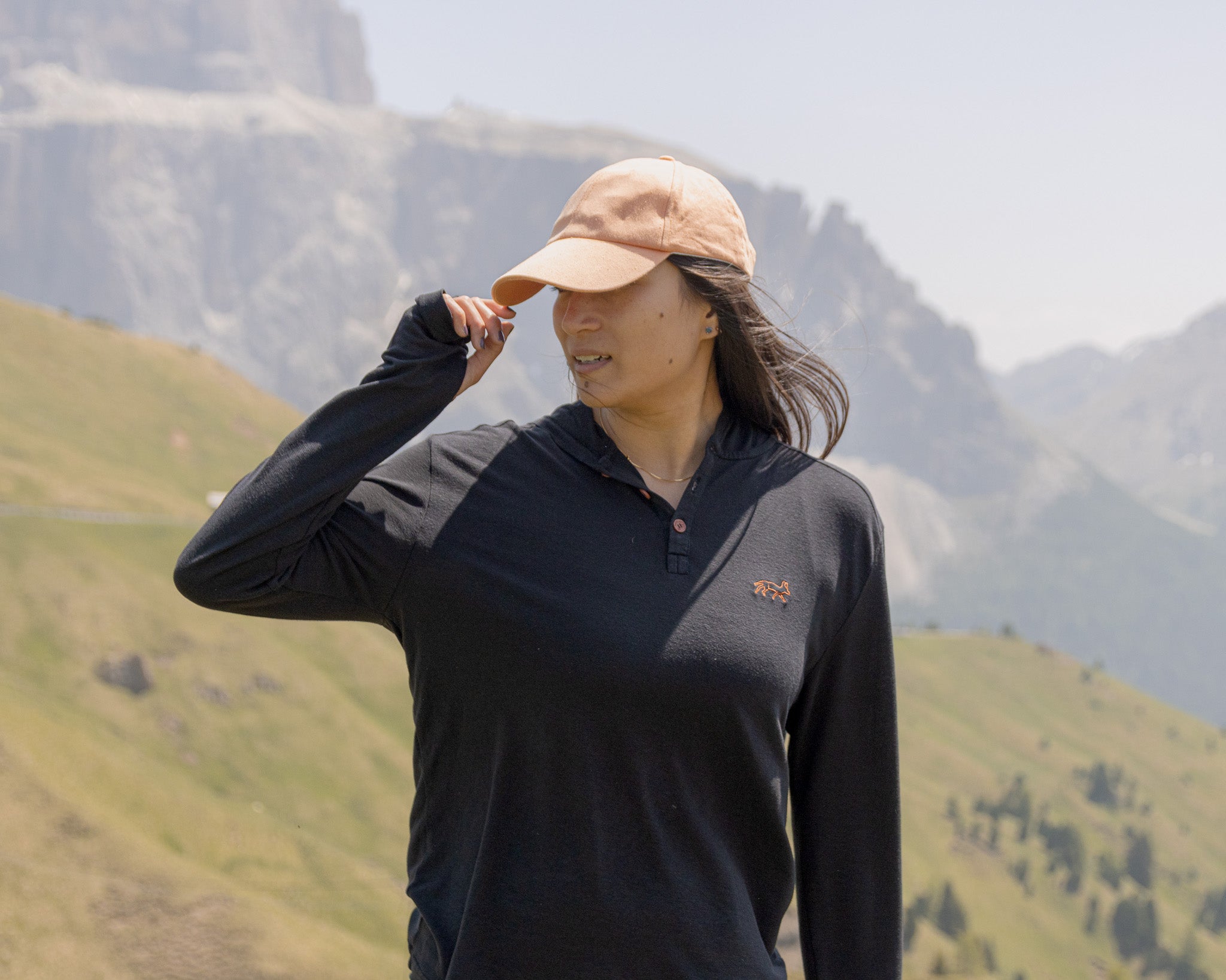 White Sands - Women's Long-Sleeve Hooded Henley in Obsidian (Black), person standing in a mountainous landscape.