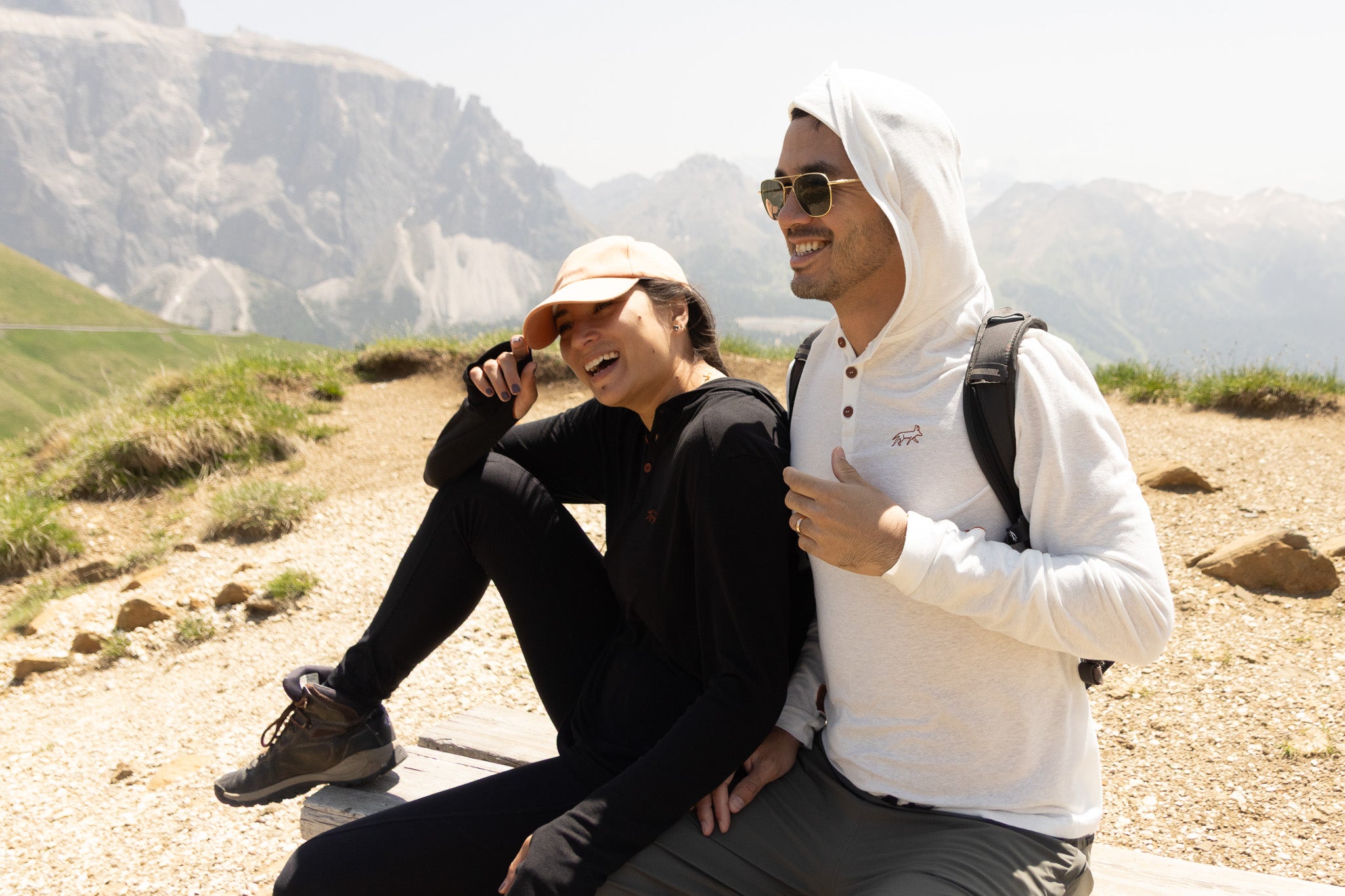 Two people sitting on a rocky path with mountains in the background