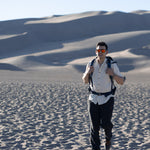 Man with a backpack in the dunes with a scenic view wearing Everglades - Men's Short-Sleeve Shirt in Chamisa (Tan) (front view)
