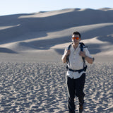 Man with a backpack in the dunes with a scenic view wearing Everglades - Men's Short-Sleeve Shirt in Chamisa (Tan) (front view)