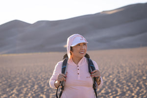 White Sands - Women’s Long-Sleeve Hooded Henley in Prickly Pear (Dusty Pink) (Front view in the sands and backpack) 