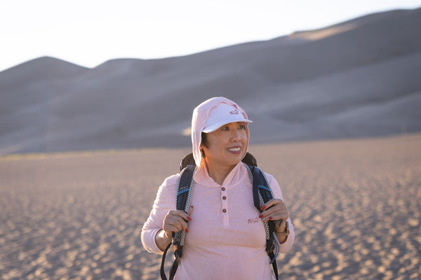 White Sands - Women’s Long-Sleeve Hooded Henley in Prickly Pear (Dusty Pink) (Front view in the sands and backpack) 