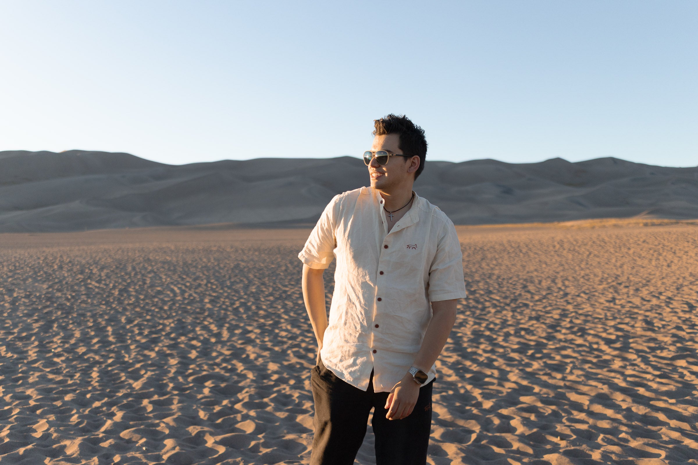 Man with a backpack in the dunes with a scenic view wearing Everglades - Men's Short-Sleeve Shirt in Chamisa (Tan) (front view)
