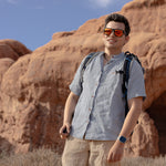Man with a backpack standing on a rocky landscape with a scenic view wearing Everglades - Men's Short-Sleeve Shirt in Blue Sage (Light Blue) (front view)