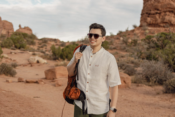 Man with a backpack standing in a desert landscape with rock formations.