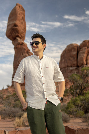 Man with a backpack standing on a rocky landscape with a scenic view wearing Everglades - Men's Short-Sleeve Shirt in Chamisa (Tan) (front view)
