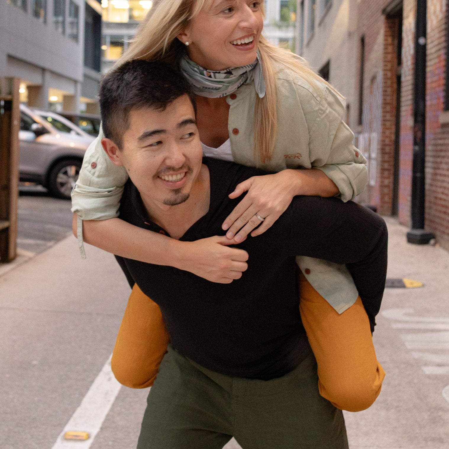Man giving a woman a piggyback ride on a city street.