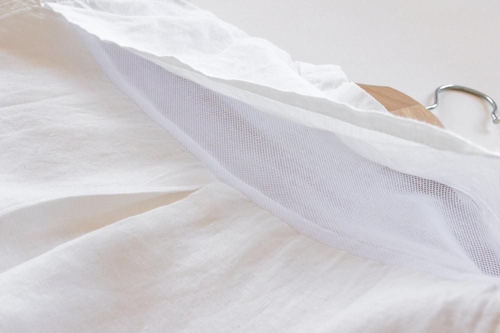 White wedding dress with sheer overlay on a hanger against a light background