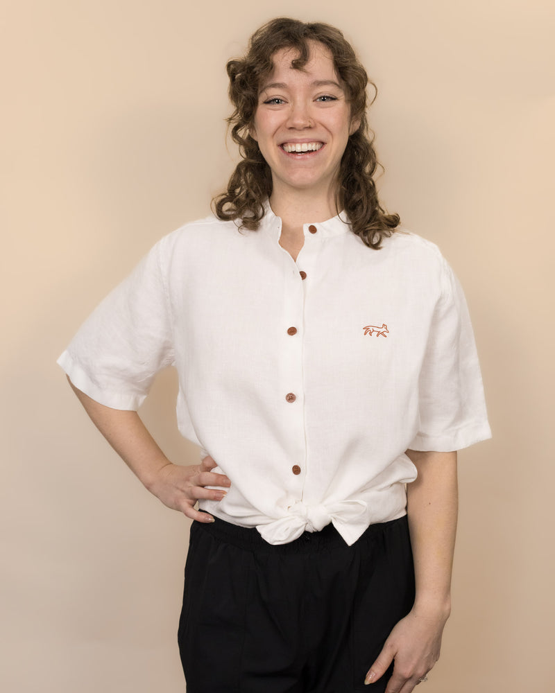 Person wearing a white shirt with brown buttons against a beige background