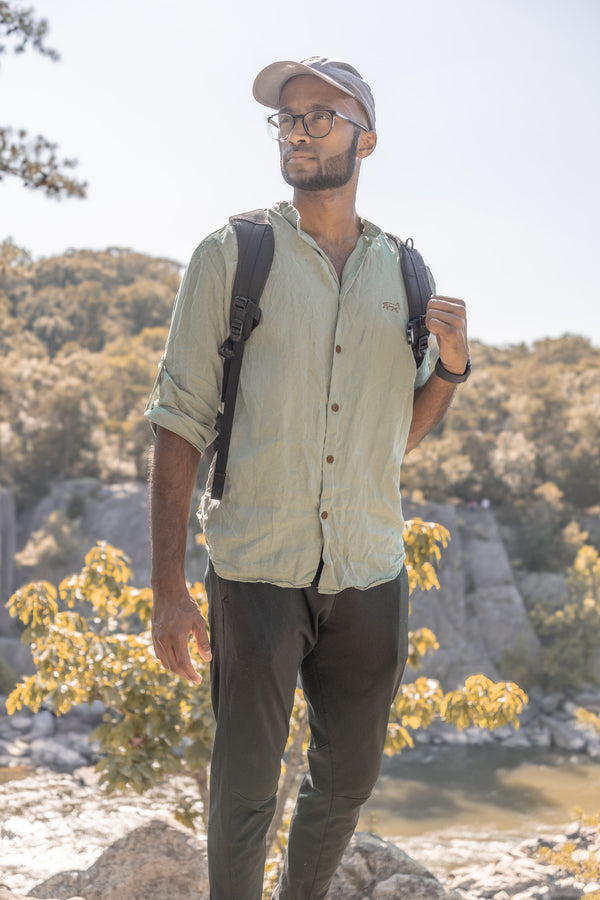 Man with a backpack standing outdoors near a body of water with trees in the background