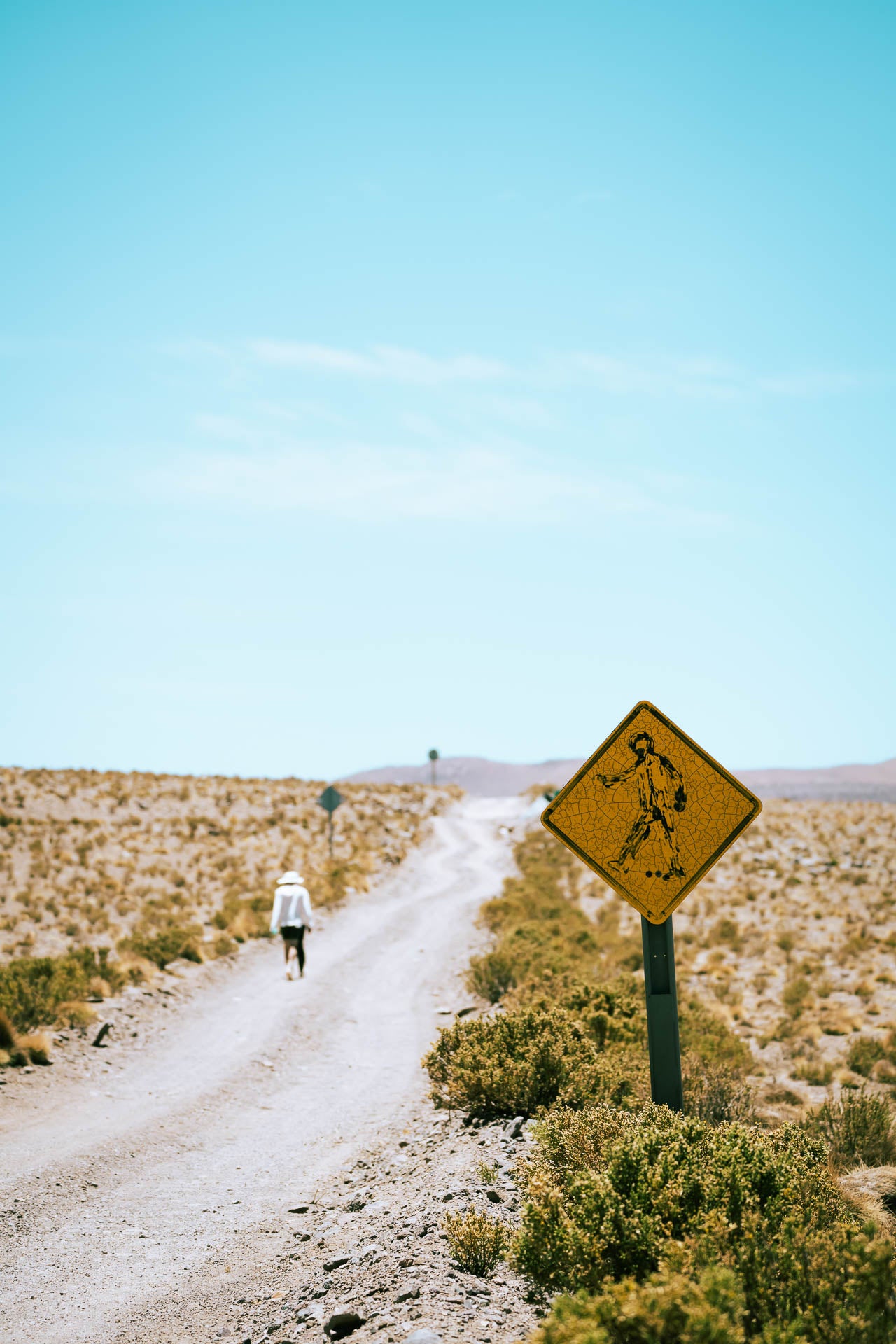 Desert road with a warning sign and person walking in the distance